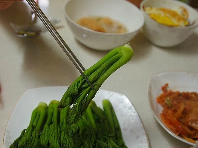 밥상에서 젓가락으로 데친 두릅을 집어 드는 모습.
